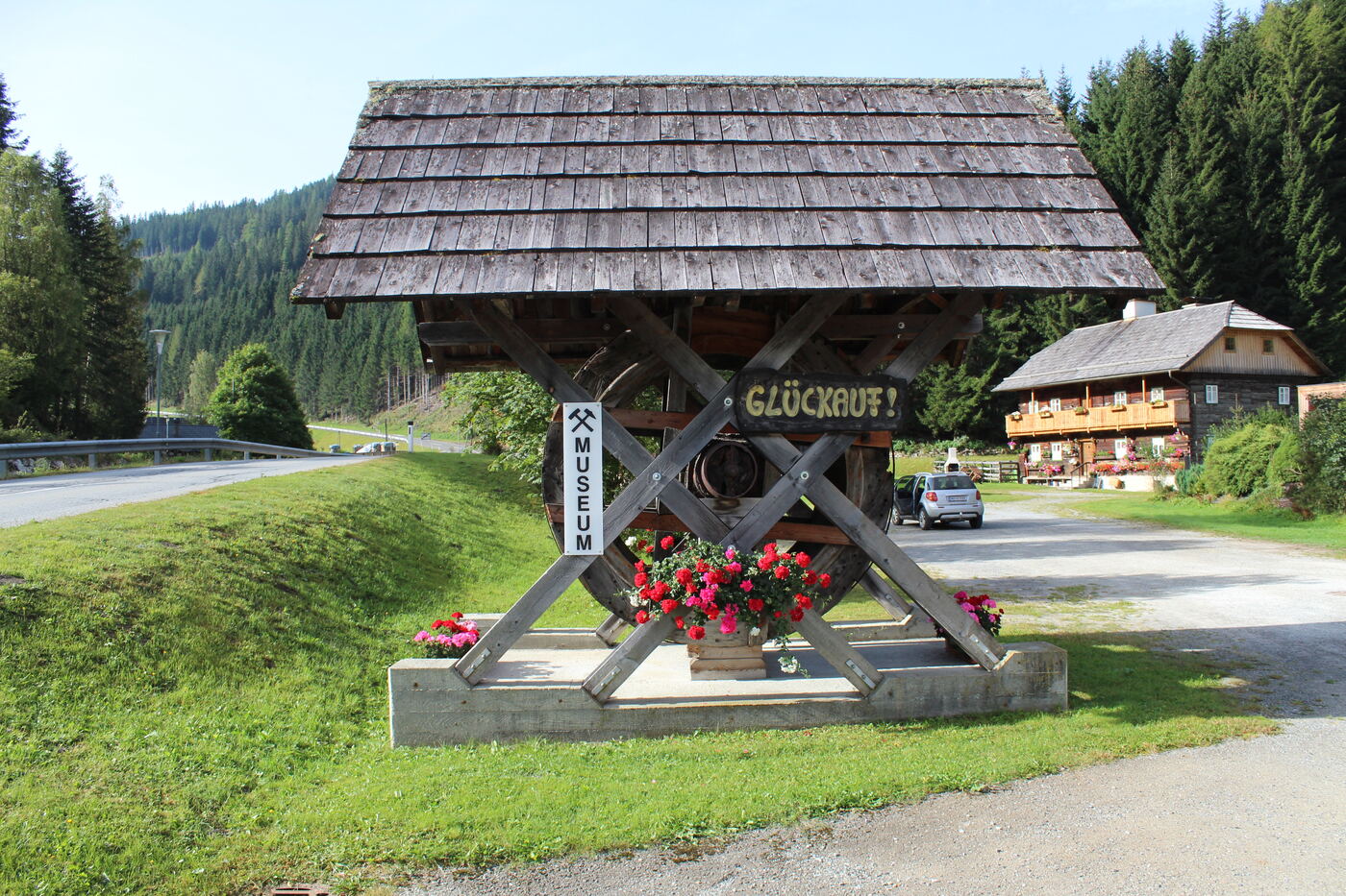 Wasserrad mit Schild „Glückauf!“ und Hinweis Museum an der Einfahrt