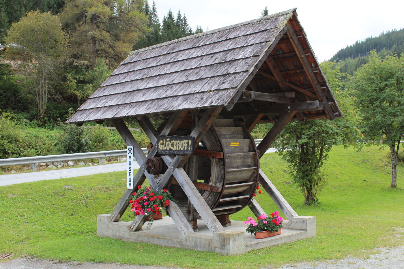 Wasserrad unter Schindeldach mit Schild „Glückauf!“